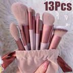 Set of 13 makeup brushes in pink and beige handles with a drawstring bag on a fluffy white background.