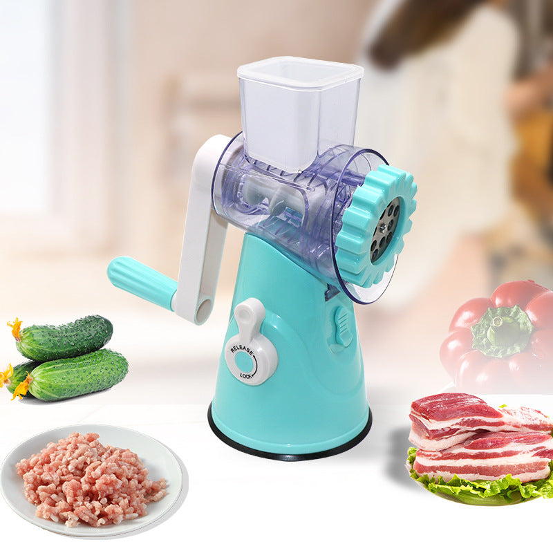 Turquoise manual meat grinder with ingredients like cucumbers, ground meat, and pork slices on a blurred background.
